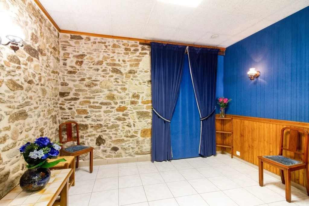 Salon funéraire avec mur en pierre apparente, rideaux en velours bleu et décoration florale
